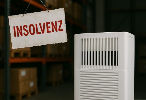 Ein weißer Luftreiniger steht in einem Lagerraum mit gestapelten Kartons auf Metallregalen. Daneben hängt ein Schild mit der Aufschrift ‚INSOLVENZ‘ in roten Buchstaben. Die Szene wirkt nüchtern und symbolisiert die wirtschaftliche Notlage des Unternehmens